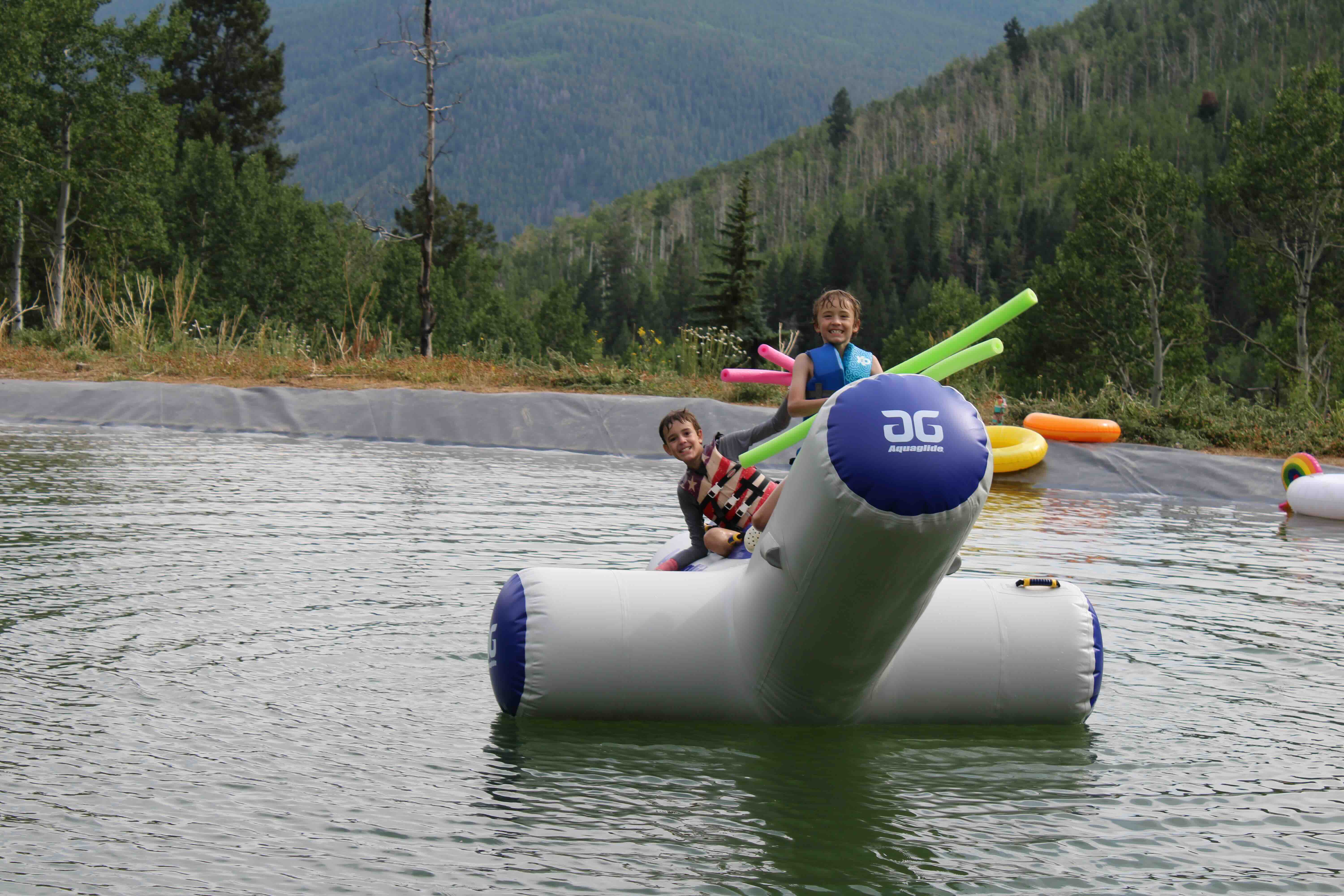 Campers on the pond water toy with the mountains behind at Ajax Sleepaway